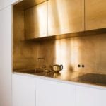 10-a-polished-gold-kitchen-backsplash-and-upper-cabinets-create-a-glam-minimalist-look-in-the-white-kitchen