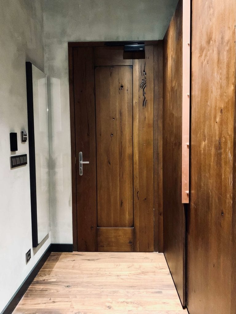 drewniane-drzwi-do-pokoju-w-hotelu-warszawa-betonowe-ściany-lustro-włoskie marki-drewniana-podłoga-szafa